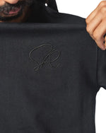 Black core t-shirt with a signature logo held by a person