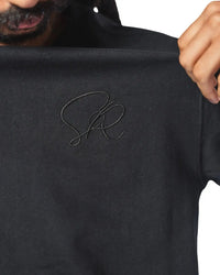 Black core t-shirt with a signature logo held by a person