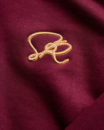 Close-up of a gold embroidered design on a crimson sweatshirt fabric background
