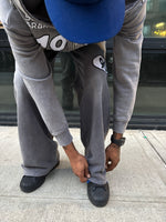 Person wearing grey90 sweatpants and a blue cap, tying their shoe on a sidewalk.