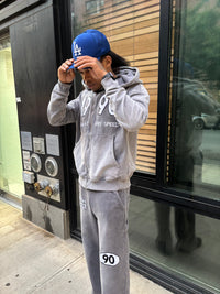 Person wearing the grey90 tracksuit and blue cap with 'LA' logo, standing outside a building.