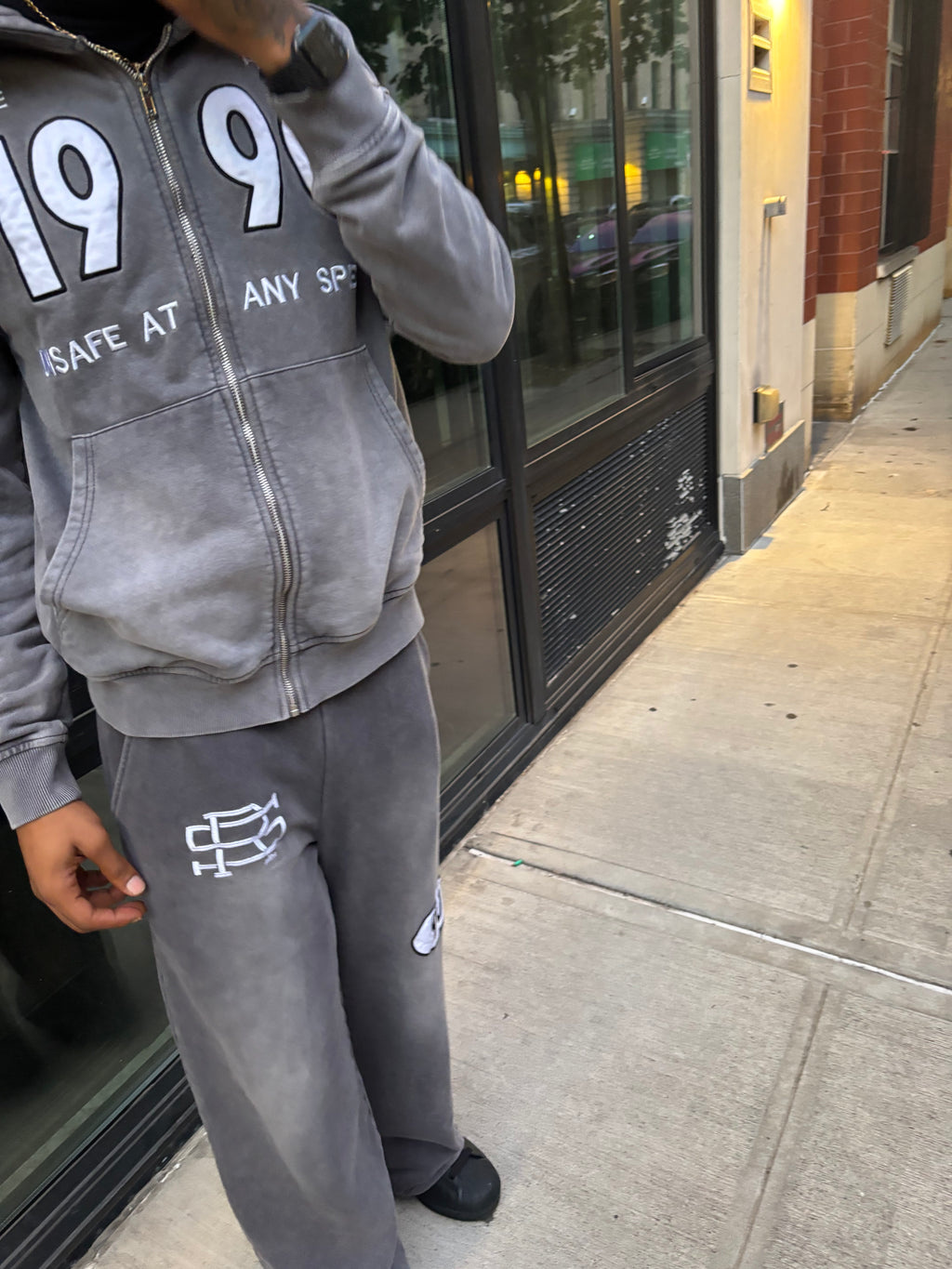 Person wearing the grey90 streetwear sweatshirt and pants with 3D embroidery and logos on a sidewalk.