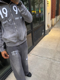 Person wearing the grey90 streetwear sweatshirt and pants with 3D embroidery and logos on a sidewalk.