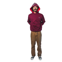 A person wearing a reversible hoodie with the hood on, showcasing a red the crimson side, paired with brown pants.